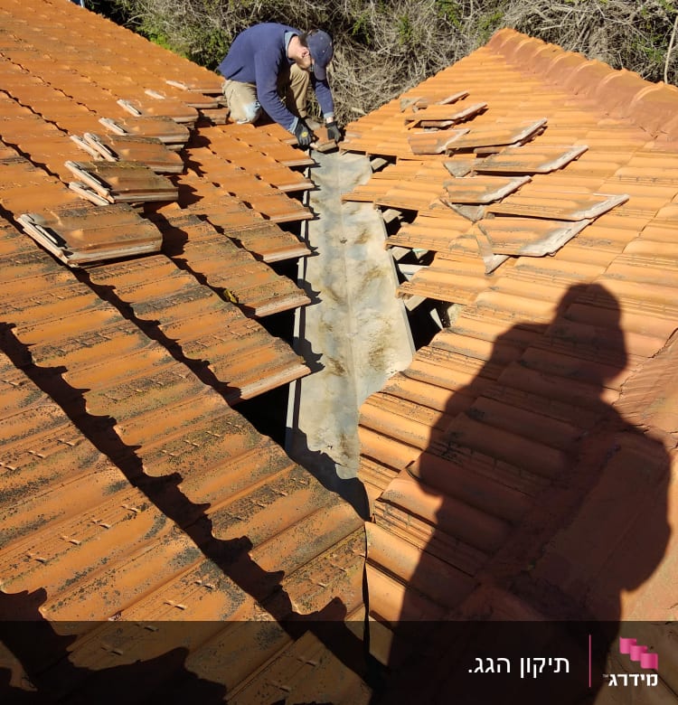 אדם מתקן רעפים על גג רעפים אדום